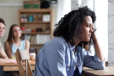 Teen girl, looking stressed, props up head with her left arm, left arm placed on desk